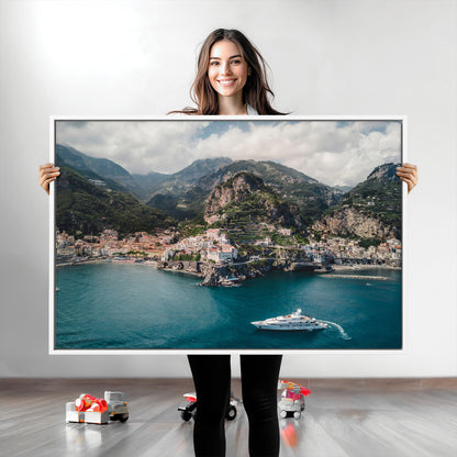 Aerial view of Amalfi Coast, Italy, with colorful hillside houses, lush green mountains, and a luxury yacht sailing in turquoise waters.