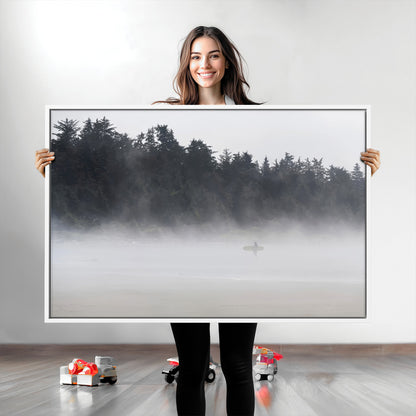A lone surfer carrying a board through a misty shoreline, surrounded by dense trees and fog, creating a peaceful and mysterious coastal scene.