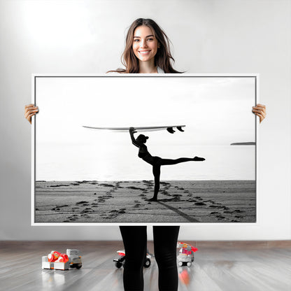 A woman balances a surfboard on her head while striking a yoga pose on the beach, silhouetted against a calm ocean horizon.