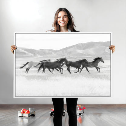 A black and white image of wild horses running freely across an open grassland, capturing the power and beauty of untamed nature in a rustic western setting.
