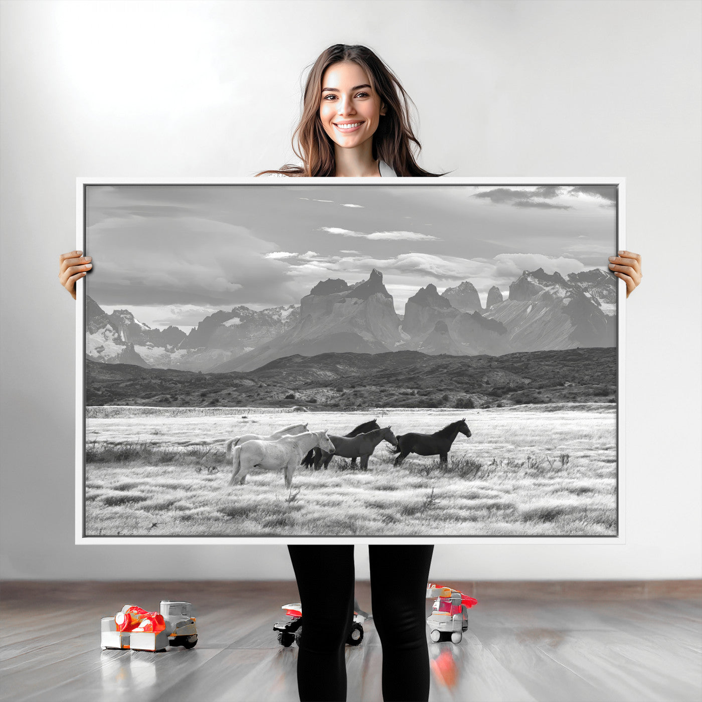 A black and white landscape of wild horses grazing in a vast grassland with towering mountains in the background, creating a moody and rustic western aesthetic.