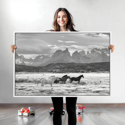 A black and white landscape of wild horses grazing in a vast grassland with towering mountains in the background, creating a moody and rustic western aesthetic.