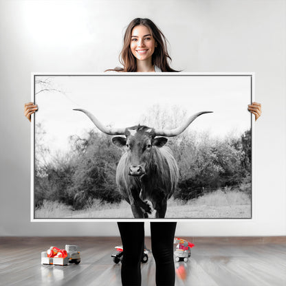 Black and white photo of a longhorn cow in a field, perfect for rustic farmhouse or western-themed interior wall decoration.