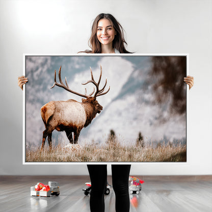 Majestic elk with large antlers standing in grass with snowy mountains in background, perfect for rustic cabin or lodge style decor.