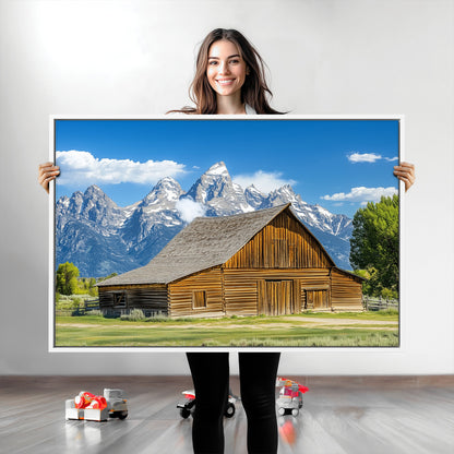 A rustic wooden barn sits in front of towering mountain peaks under a clear blue sky, perfect for farmhouse or cabin style interiors.