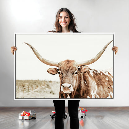 A Texas longhorn bull with wide horns, standing in a dry field under soft light, ideal for rustic farmhouse or western-themed interiors.