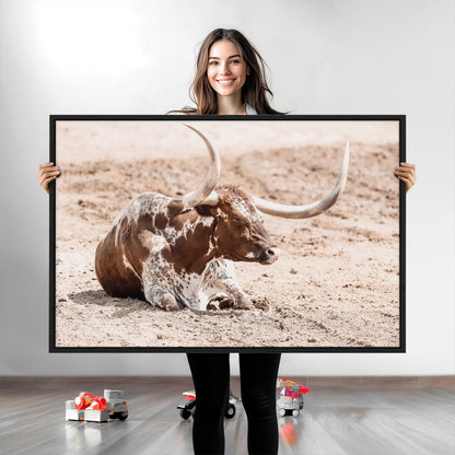 Texas Longhorn bull resting on dusty ground with warm tones, ideal for rustic western or farmhouse-themed wall decor.