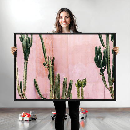 Framed canvas of tall green cacti against a soft pink wall, ideal for modern desert or colorful southwest-inspired home decor.
