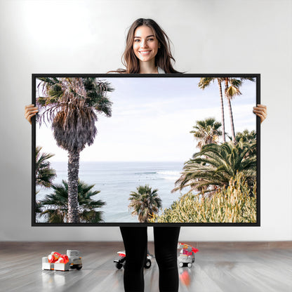 Scenic coastal view with tall palm trees overlooking a calm ocean, soft blue waves, and surfers in the distance, creating a peaceful tropical vibe.