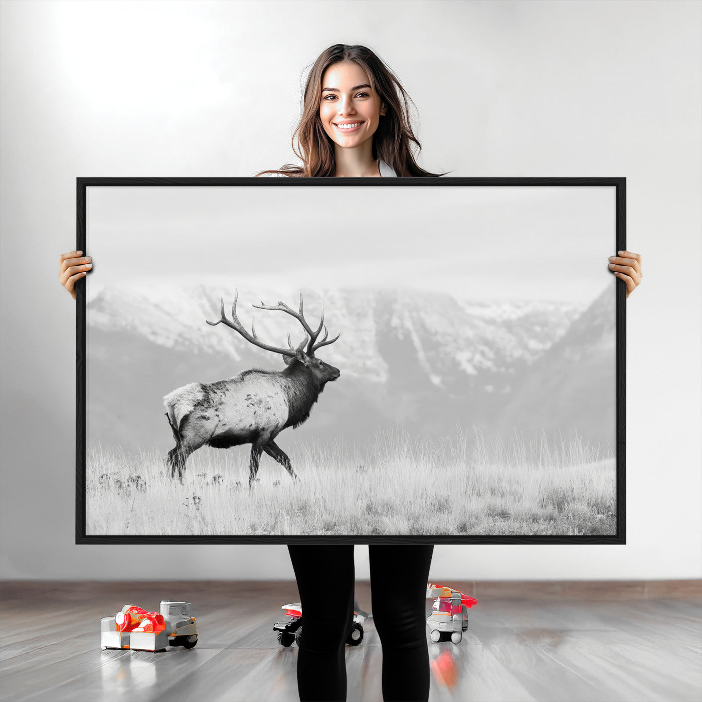 Black and white photograph of a majestic elk standing in a grassy field with snow-capped mountains in the background, creating a bold and rustic wilderness scene.