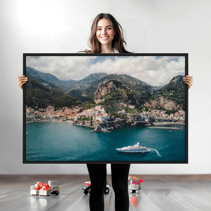 Aerial view of Amalfi Coast, Italy, with colorful hillside houses, lush green mountains, and a luxury yacht sailing in turquoise waters.