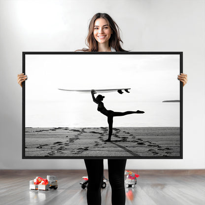 A woman balances a surfboard on her head while striking a yoga pose on the beach, silhouetted against a calm ocean horizon.