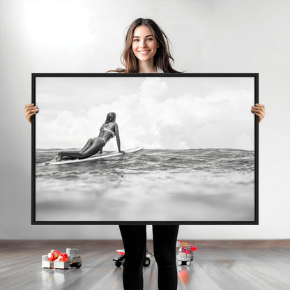 A black and white ocean scene featuring a surfer girl waiting on her board, gazing at the horizon, capturing a tranquil and adventurous coastal moment.