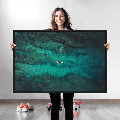 An aerial view of a solo surfer paddling through crystal-clear turquoise waters over a sunlit reef, capturing the beauty and serenity of open water surfing.