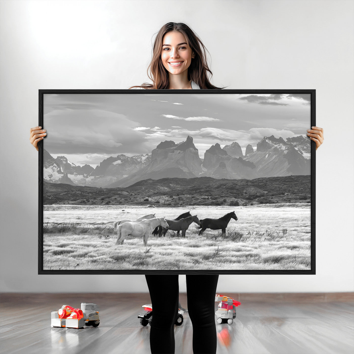 A black and white landscape of wild horses grazing in a vast grassland with towering mountains in the background, creating a moody and rustic western aesthetic.