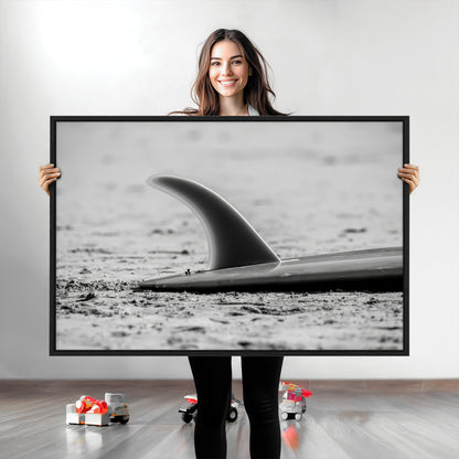 A black and white close-up of a surfboard fin resting on the sandy shore, highlighting minimalist beach aesthetics and classic surf culture.