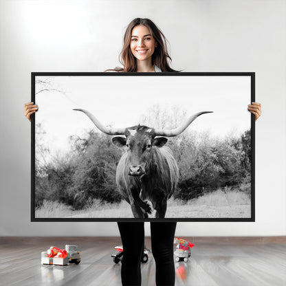 Black and white photo of a longhorn cow in a field, perfect for rustic farmhouse or western-themed interior wall decoration.