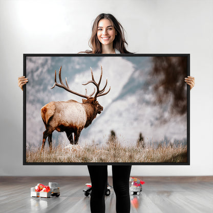 Majestic elk with large antlers standing in grass with snowy mountains in background, perfect for rustic cabin or lodge style decor.