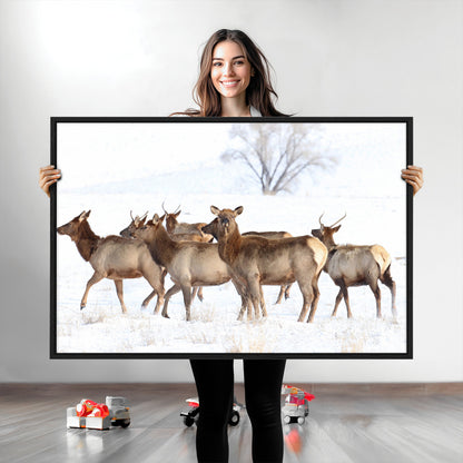 A group of elk standing on snowy terrain with a tree in the background, perfect for rustic or lodge-style winter wall decor.
