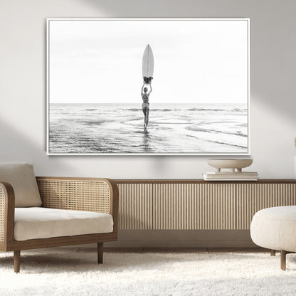 Black and white image of a female surfer holding a surfboard above her head while walking toward the ocean, creating a minimalist and bold coastal aesthetic.