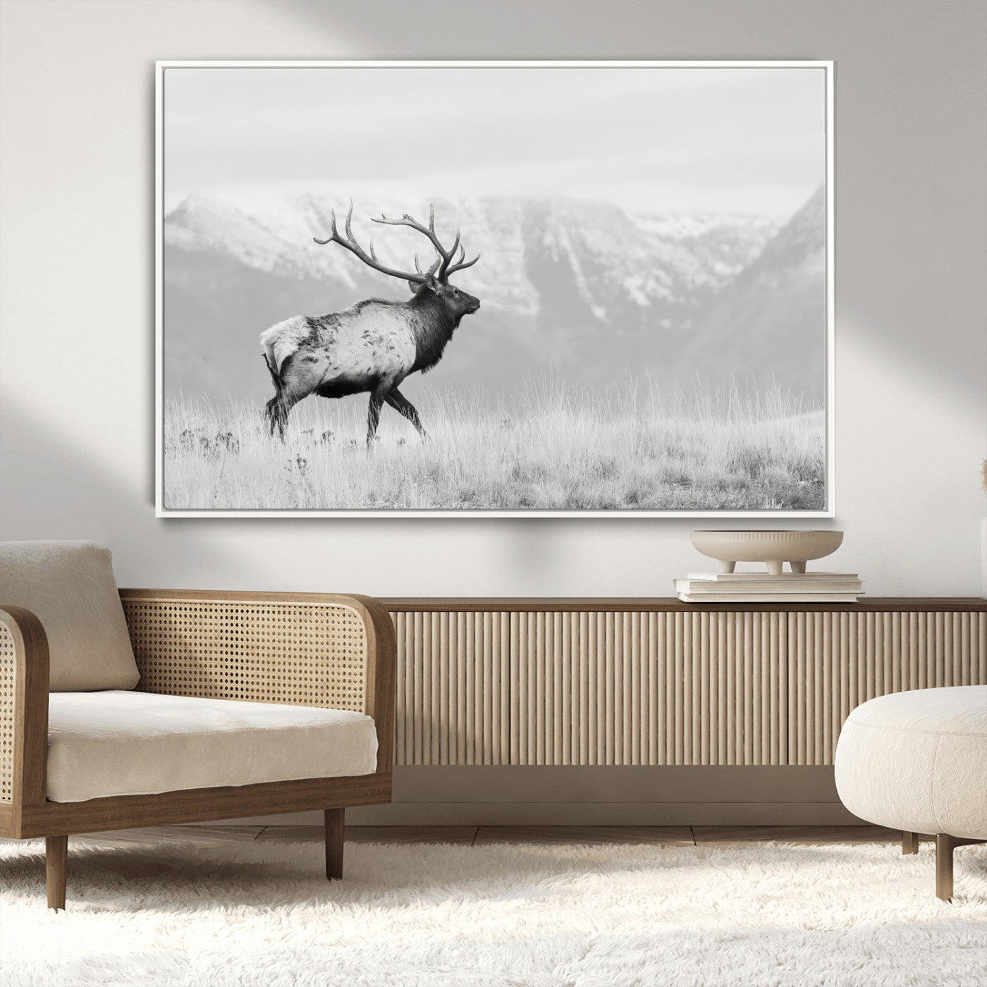 Black and white photograph of a majestic elk standing in a grassy field with snow-capped mountains in the background, creating a bold and rustic wilderness scene.