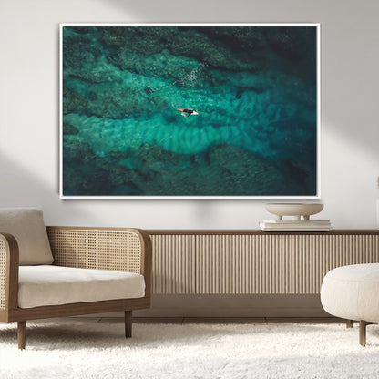 An aerial view of a solo surfer paddling through crystal-clear turquoise waters over a sunlit reef, capturing the beauty and serenity of open water surfing.