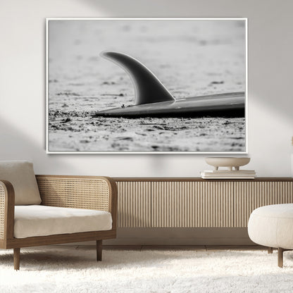 A black and white close-up of a surfboard fin resting on the sandy shore, highlighting minimalist beach aesthetics and classic surf culture.