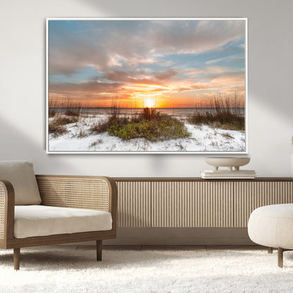 A tranquil beach scene featuring golden sunset hues over the water, with grasses in the foreground and a peaceful, serene atmosphere.