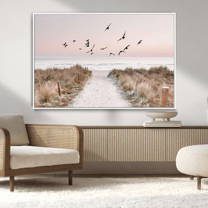 A peaceful coastal pathway leading to the ocean, with birds flying across a soft pastel sky, creating a calm and scenic beach atmosphere.