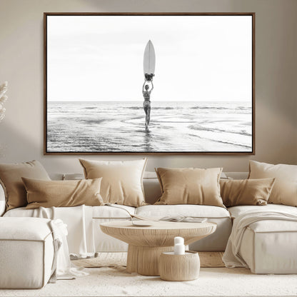 Black and white image of a female surfer holding a surfboard above her head while walking toward the ocean, creating a minimalist and bold coastal aesthetic.