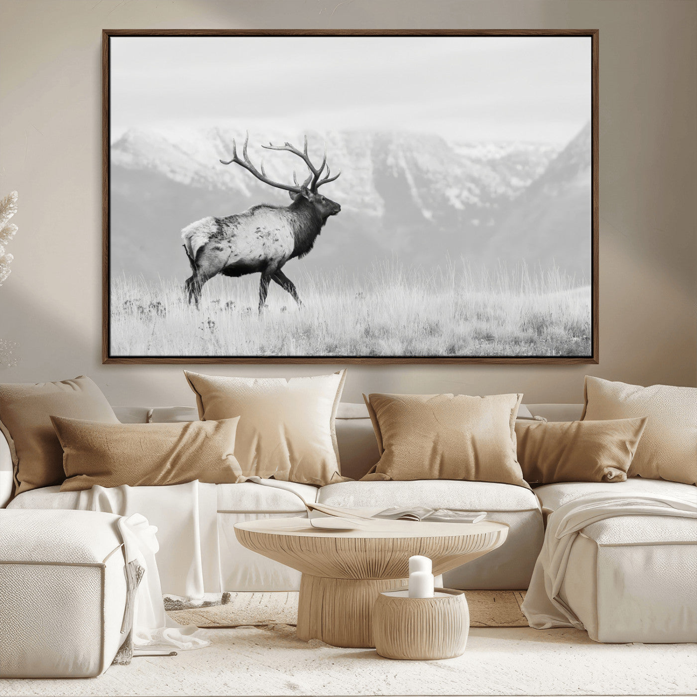 Black and white photograph of a majestic elk standing in a grassy field with snow-capped mountains in the background, creating a bold and rustic wilderness scene.