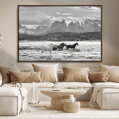 A black and white landscape of wild horses grazing in a vast grassland with towering mountains in the background, creating a moody and rustic western aesthetic.