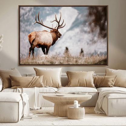 Majestic elk with large antlers standing in grass with snowy mountains in background, perfect for rustic cabin or lodge style decor.