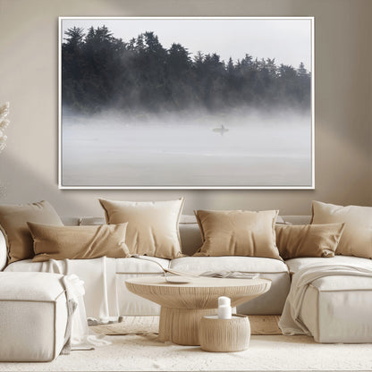 A lone surfer carrying a board through a misty shoreline, surrounded by dense trees and fog, creating a peaceful and mysterious coastal scene.