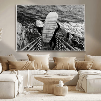 Black and white photo of surfers carrying boards down a rugged cliffside stairway, capturing a bold and adventurous coastal scene.