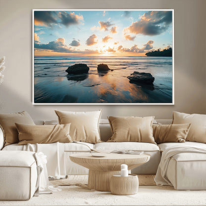 A serene beach at sunset with vibrant clouds, calm water, and rocks in the foreground reflecting the warm colors of the setting sun.