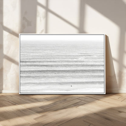 Monochrome photo of a lone surfer in calm layered waves, perfect for minimalist coastal or moody ocean-inspired wall decoration.
