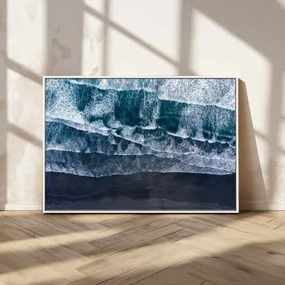Canvas of aerial ocean waves crashing onto a black sand beach in moody tones, ideal for modern coastal or minimalist home decor.