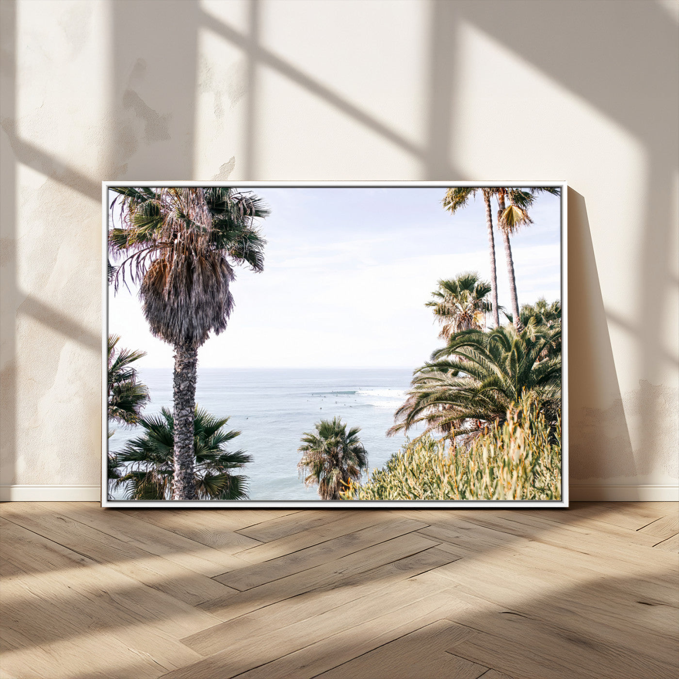 Scenic coastal view with tall palm trees overlooking a calm ocean, soft blue waves, and surfers in the distance, creating a peaceful tropical vibe.