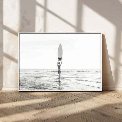 Black and white image of a female surfer holding a surfboard above her head while walking toward the ocean, creating a minimalist and bold coastal aesthetic.