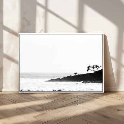Black and white photo of a surfer standing on rocky cliffs, gazing at the waves, embodying the spirit of adventure and solitude.