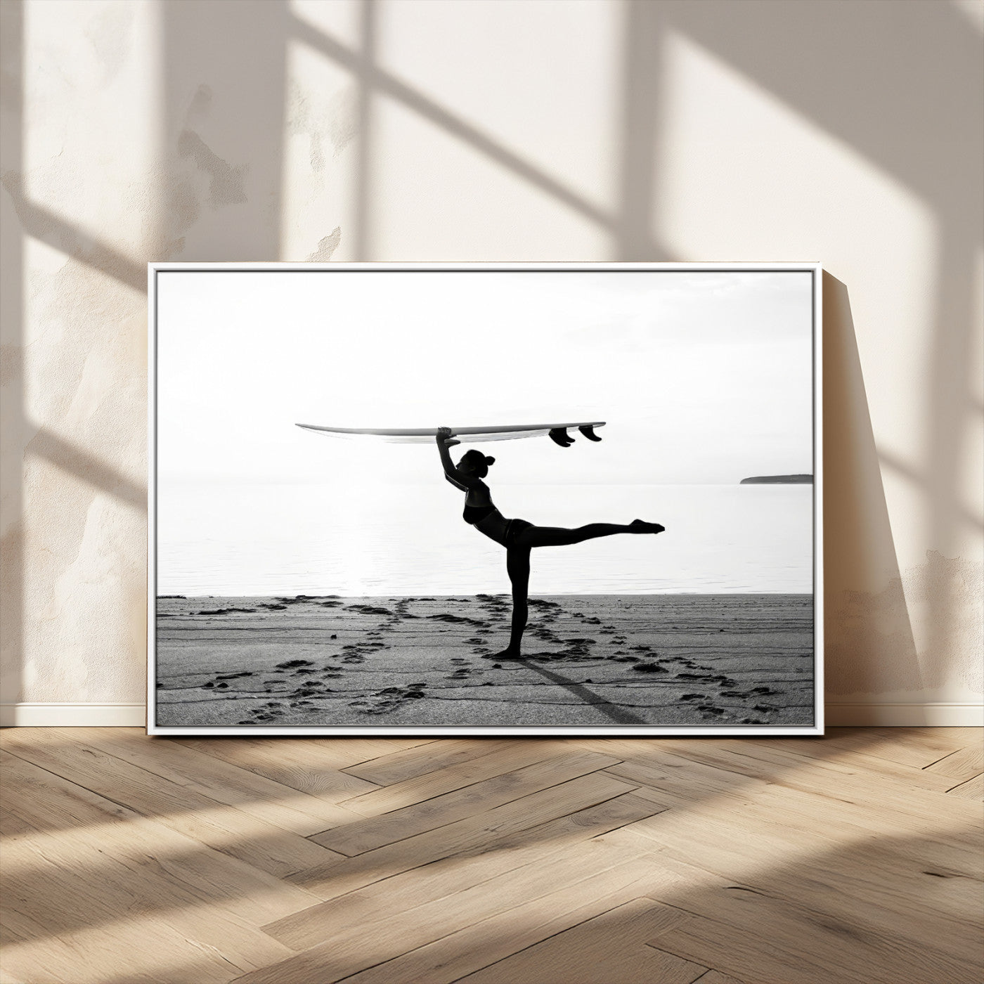 A woman balances a surfboard on her head while striking a yoga pose on the beach, silhouetted against a calm ocean horizon.