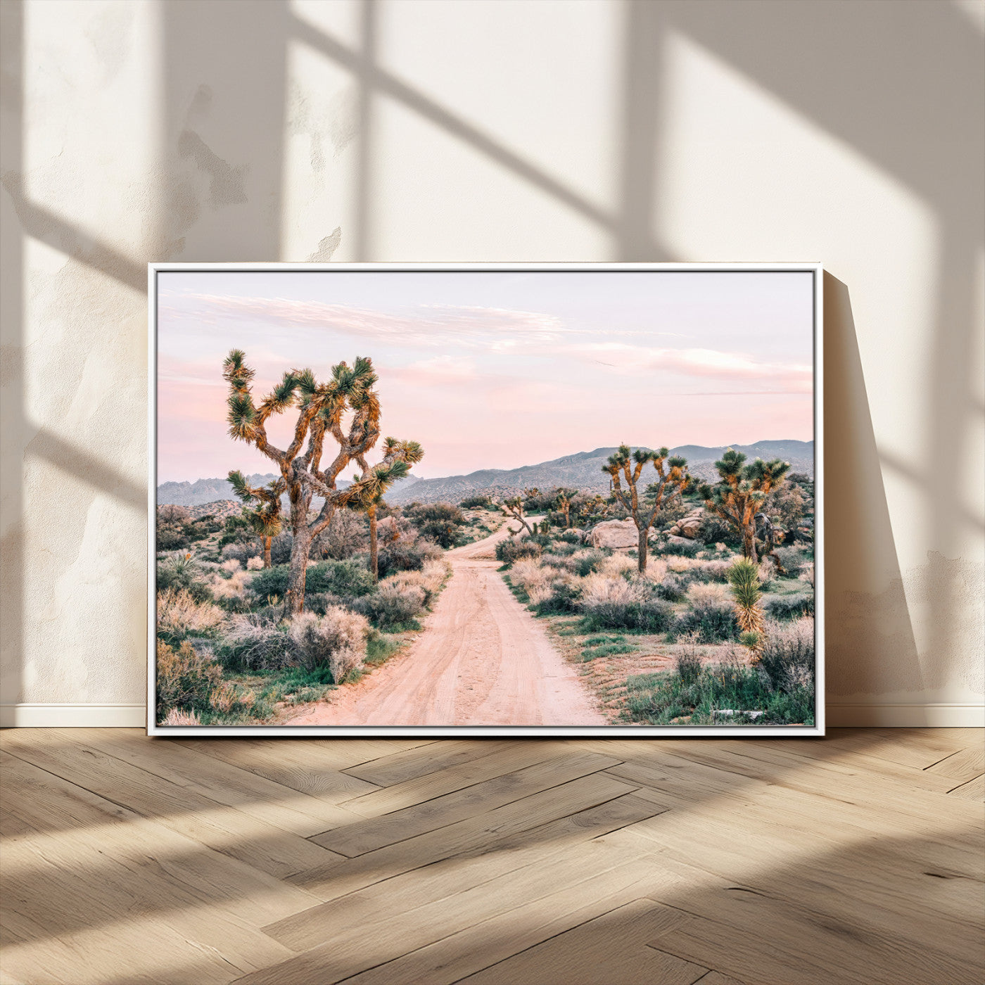 A dusty road winding through Joshua Tree National Park, framed by iconic twisted trees and warm desert tones under a soft pastel sky.