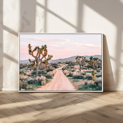 A dusty road winding through Joshua Tree National Park, framed by iconic twisted trees and warm desert tones under a soft pastel sky.