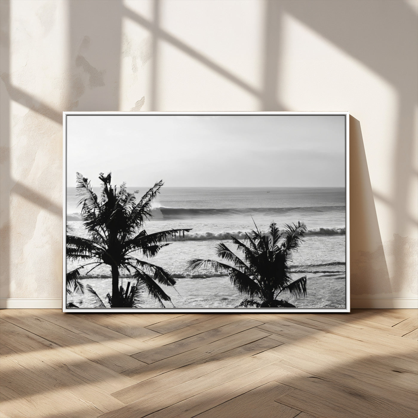 Black and white view of ocean waves crashing on a tropical coastline, framed by silhouetted palm trees under a vast, open sky.