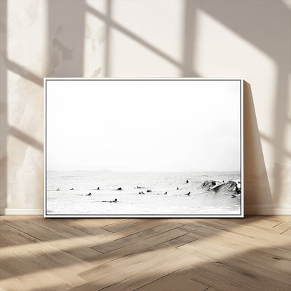 A group of surfers floating in the ocean, waiting for waves under a vast, moody sky, captured in black and white.