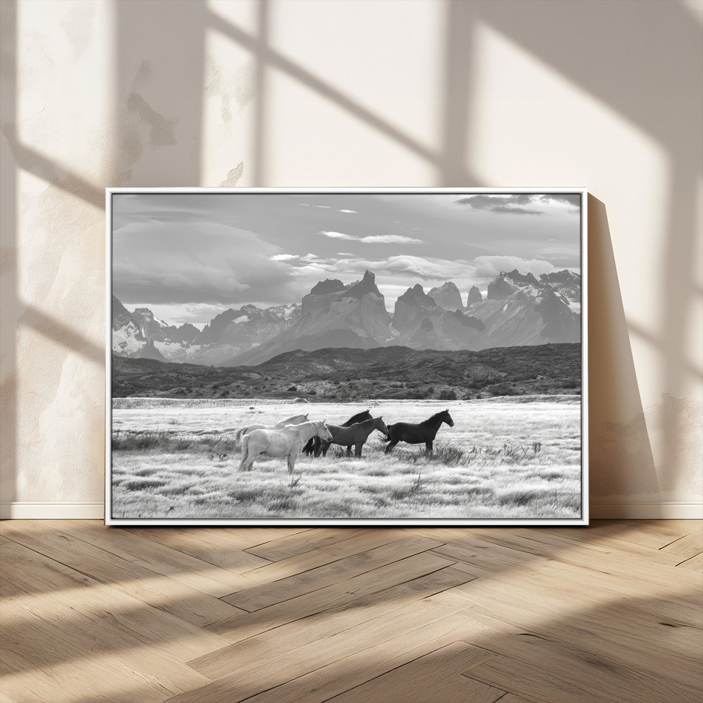 A black and white landscape of wild horses grazing in a vast grassland with towering mountains in the background, creating a moody and rustic western aesthetic.
