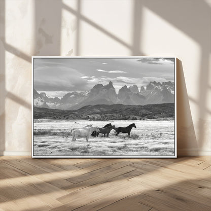 A black and white landscape of wild horses grazing in a vast grassland with towering mountains in the background, creating a moody and rustic western aesthetic.