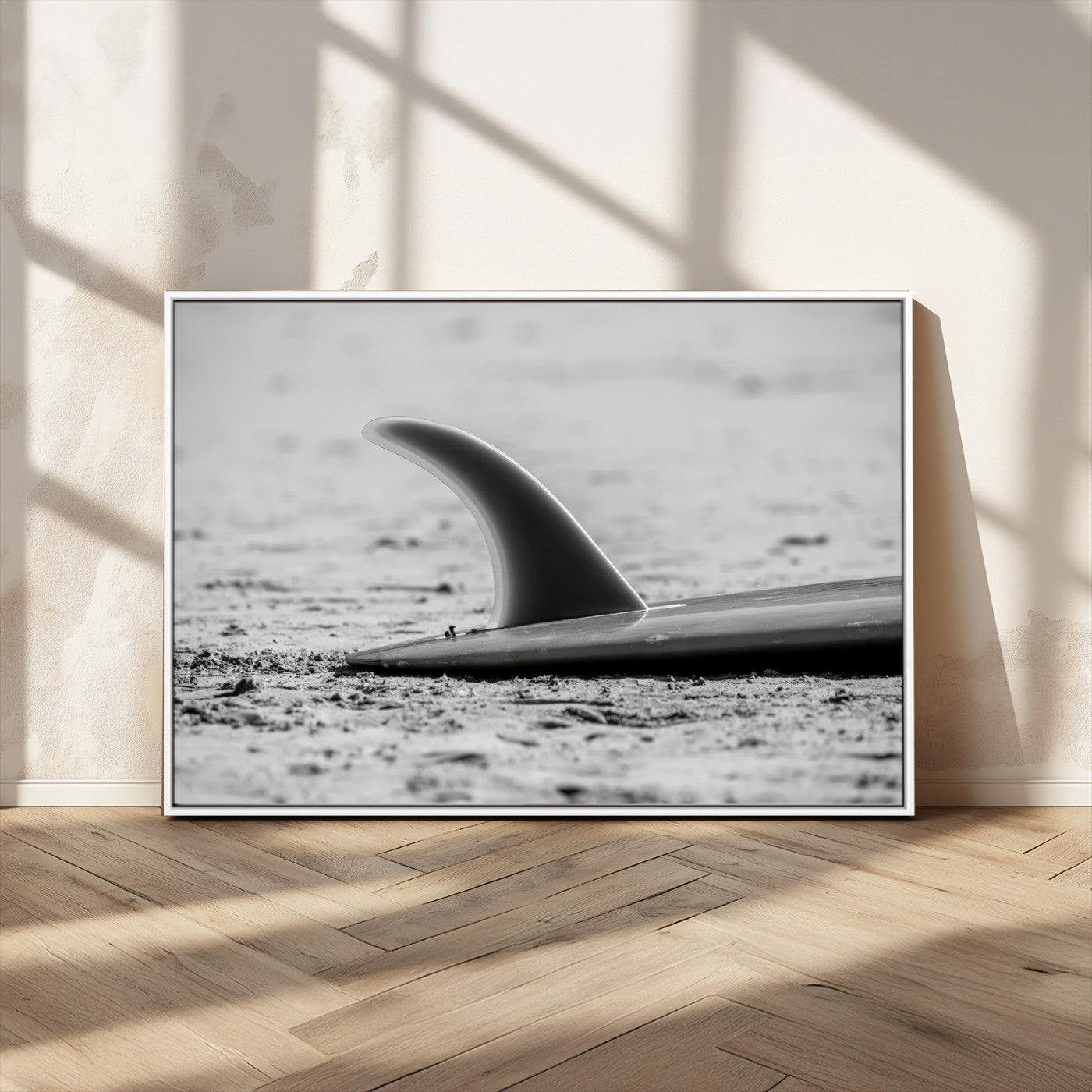 A black and white close-up of a surfboard fin resting on the sandy shore, highlighting minimalist beach aesthetics and classic surf culture.