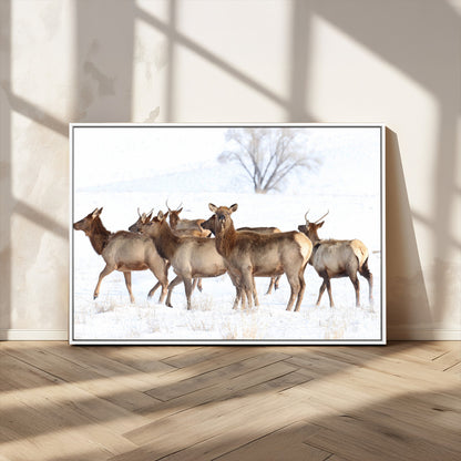 A group of elk standing on snowy terrain with a tree in the background, perfect for rustic or lodge-style winter wall decor.